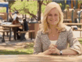 a woman is smiling while sitting at a picnic table in a park .