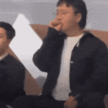 two men are standing next to each other in a room and one of them is eating something .