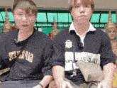 two young men are sitting next to each other with one wearing a shirt that says ' tokyo ' on the front .