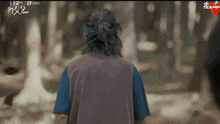 a man in a purple vest and blue shirt is walking through a forest .