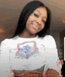 a woman wearing a white shirt with a picture of a book on it is smiling and looking at the camera .