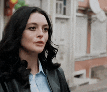 a woman wearing a blue shirt and a black jacket stands in front of a building