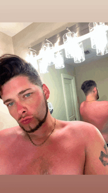 a shirtless man with a tattoo on his arm takes a selfie in front of a mirror