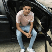 a young man in a pink adidas shirt sits in the doorway of a car