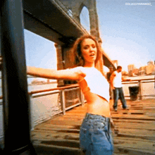 a woman in a white crop top is standing on a pier with her arms outstretched