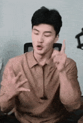 a man in a brown shirt is sitting in a chair and making a funny face with his hands .