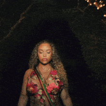 a woman in a floral top stands in front of a string of lights at night