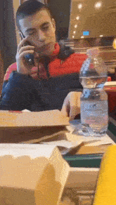 a man sits at a table talking on a cell phone while a bottle of water sits on the table
