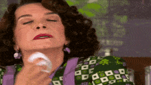 a woman wipes her face with a tissue while wearing a purple and green dress