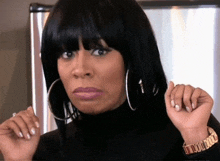 a woman wearing hoop earrings and a watch is making a face