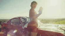 a shirtless man is washing a red car