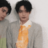 two young men are standing next to each other and one of them is wearing a sweater and a tie .