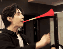 a man in a black shirt is blowing a red trumpet in his mouth