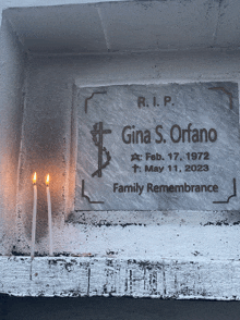 two candles are lit in front of a plaque that says r.i.p gina s. orfano