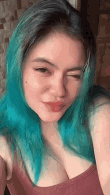 a woman with blue hair is taking a selfie while wearing a pink tank top .