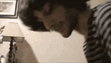 a man in a striped shirt is looking down at something in front of a lamp