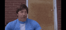 a man in a blue shirt and white shirt is sitting in front of a brick building .