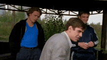 three men are standing next to each other in a gazebo . one of the men is wearing a blue shirt .