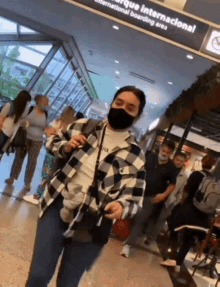a woman wearing a mask stands in front of a sign that says parque internacional international boarding area