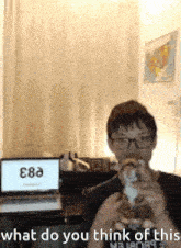 a boy with glasses is drinking a cup of coffee in front of a laptop and a map .