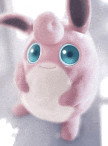 a pink and white stuffed animal with blue eyes looks at the camera