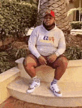 a man is sitting on a set of stairs wearing a sweatshirt that says ezus .