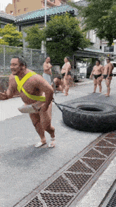 a sumo wrestler is pulling a tire down the street