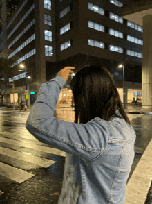 a woman in a denim jacket is standing on a wet street