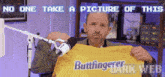 a man is holding up a yellow shirt that says buttfinger dark web