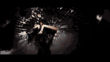 a woman in a black dress is standing in a dark room with her hands together .