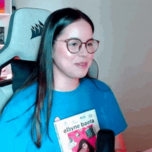 a woman wearing glasses and a blue shirt is holding a book called elayne baeta