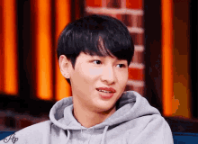 a young man wearing a grey hoodie is sitting on a couch and smiling .