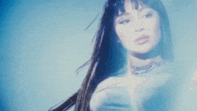 a woman with long hair is standing in front of a blue background and looking at the camera .