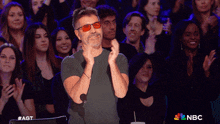 a man wearing red glasses applauds in front of a crowd that is applauding