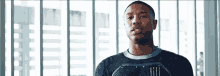 a man in a black shirt is standing in front of a window and looking at the camera .