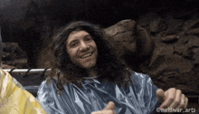 a man with long curly hair is wearing a plastic poncho and smiling for the camera