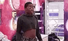 a young woman wearing a crop top and glasses is standing in a room .