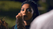 a woman with blue hair is touching her face .