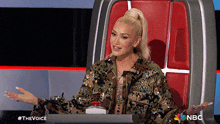 a woman in a camouflage jacket is sitting in a chair with nbc written on it