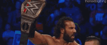 a man with a beard is holding a wrestling championship belt in the air in front of a crowd .