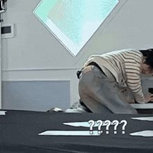 a man in a striped shirt is kneeling down on a table with a question mark on the floor .