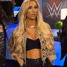 a blonde woman wearing a leopard print jacket and a black bra is standing in front of a w logo .