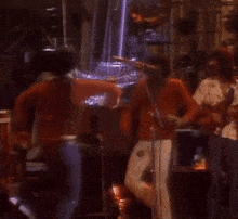 a man in an orange jacket and white pants is dancing on stage