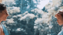 a man and a woman are standing next to each other in front of a forest .