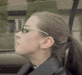 a woman wearing glasses and a ponytail is sitting in a car looking out the window .