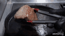 a person is cooking a piece of meat in a frying pan with tongs and the words made in animatica at the bottom