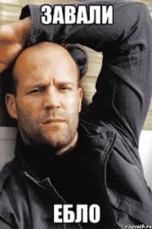 a bald man with a beard is laying on a couch with his arms over his head .