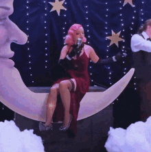 a woman in a red dress sitting on a crescent moon