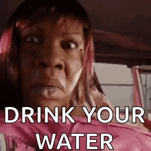 a woman is sitting in a car with the words drink your water written on her face .