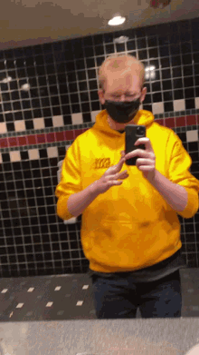 a man in a yellow hoodie taking a selfie with his phone